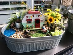 a tin pan filled with plants and flowers on top of a table next to a window