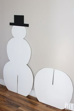 two snowmen are standing next to each other in front of a wall with a hat on top