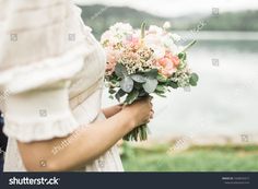 a woman holding a bouquet of flowers in her hands with water in the background on a cloudy day