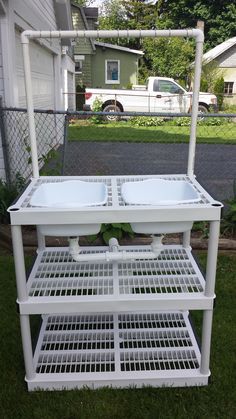 a white cart with two bowls on it sitting in the grass next to a house