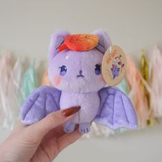 a hand holding a purple stuffed animal with an orange tag on it's ear