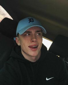 a man wearing a baseball cap sitting in the back seat of a car with his tongue out