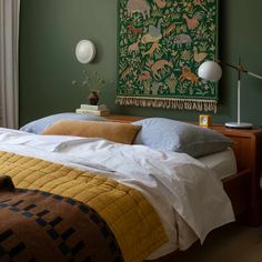 a bed in a bedroom with green walls and artwork on the wall above it,