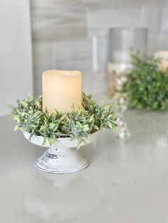 a lit candle sitting on top of a white bowl filled with greenery next to candles