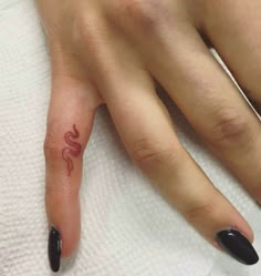 a woman's hand with a snake tattoo on her left thumb and black nails