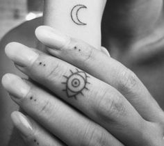 two hands with small tattoos on them holding each other's fingers and one has an eye