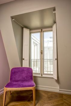 a purple chair sitting in front of a window on top of a hard wood floor