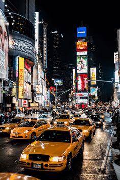 a busy city street filled with yellow cabs and tall buildings at night time in new york