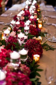 the long table is set with candles and flowers on it, along with wine glasses