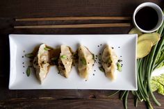 three dumplings on a white plate with chopsticks next to them and a cup of coffee