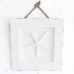 a white frame hanging on the wall with a starfish in it's center