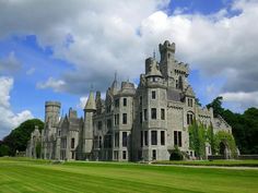 a large castle like building sitting in the middle of a lush green field under a cloudy blue sky