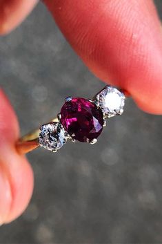 a close up of a person's hand holding an engagement ring with three stones