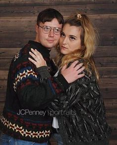 a man and woman hugging each other in front of a wooden wall