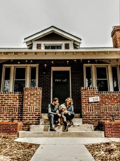 two people sitting on the front steps of a house with a dog in their lap