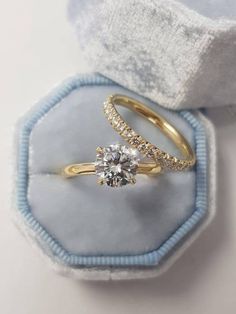 two gold engagement rings sitting in a blue velvet ring box with white and yellow diamonds on top