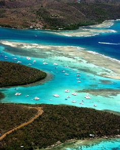 an aerial view of several boats in the water near land and trees on both sides