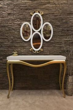 a white and gold console table in front of a brick wall with mirrors on it