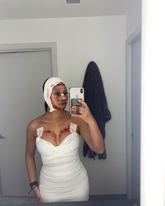 a woman in a white dress taking a selfie with her cell phone and wearing a bandage around her head