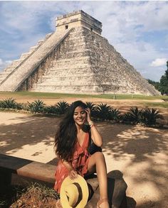 a woman sitting on a bench in front of an ancient pyramid