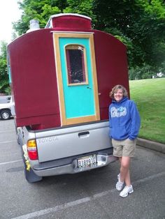 a woman standing in front of a truck with a small house on it's back