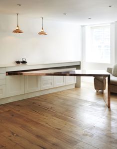 an empty kitchen with white cabinets and wood flooring is pictured in this image, there are three pendant lights hanging above the island