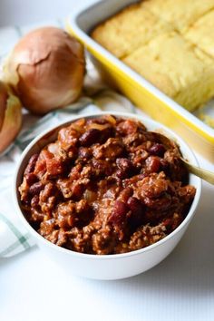 a white bowl filled with chili next to garlic and bread on top of a table