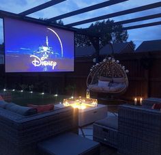 an outdoor movie screen is lit up at night with candles on the table and chairs around it