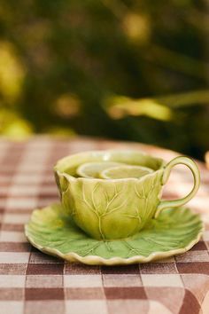 a green cup and saucer sitting on top of a checkered tablecloth covered table