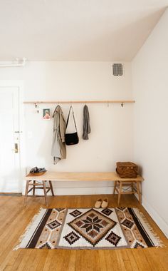 a room with a bench, coat rack and rugs on the floor in front of it