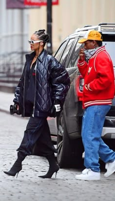 two people walking down the street in front of a car and one is talking on her cell phone