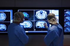 two people in scrubs looking at mri images on the wall and talking to each other