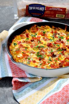 a casserole dish with ham, cheese and vegetables on a colorful towel next to a bag of bread