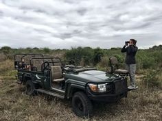 a man standing next to a green jeep in the middle of a field with people looking at it