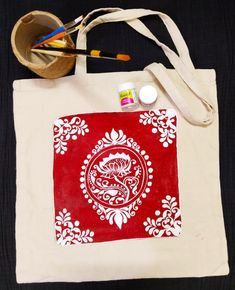 a red and white tote bag sitting on top of a table next to paintbrushes