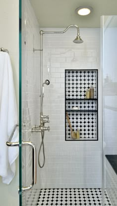 a white tiled bathroom with black and white floor tiles on the shower wall, along with two shelves holding toiletries