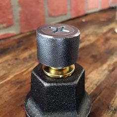 a close up of a black and gold object on a wooden table with a brick wall in the background