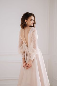 the back of a woman in a white dress with pearls on her neck and long sleeves