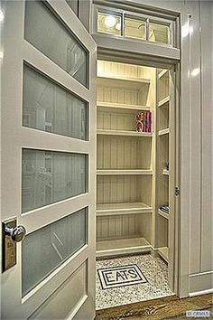 an open door leading to a walk in closet with glass doors and shelves on both sides