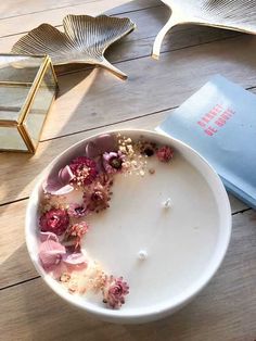 a white bowl filled with flowers on top of a wooden floor next to a book