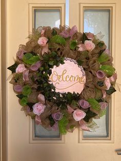 a pink and green wreath with the word welcome hanging on it's front door