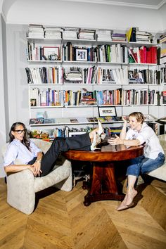 two people are sitting at a table in front of bookshelves with shelves full of books