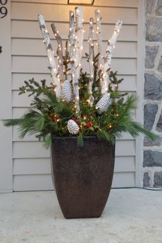 a potted plant with christmas lights and pine cones in it on the front porch