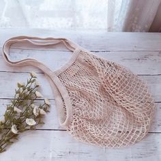 a string bag sitting on top of a white wooden floor next to a small flower