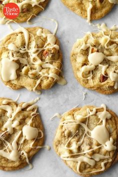 six cookies with white icing and nuts are on a sheet of baking paper,