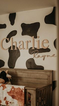 a baby crib with a teddy bear in it and the name charlie on the wall