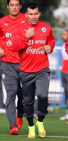 two soccer players running on the field during a training session with other players in the background