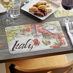 a place mat with the word italy written on it next to some wine glasses and silverware