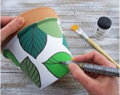 a person holding a cup with paint on it and some other items around it that are sitting on top of a wooden table