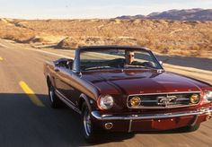 a red mustang convertible driving down the road